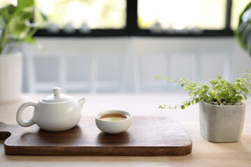 Fototapeta na wymiar Traditional east asian white teapot and cup with small green plant on wooden table 