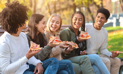 Hungry laughing teenagers enjoying pizza in park