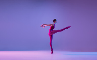 Fototapeta na wymiar Dynamic. Young and graceful ballet dancer isolated on purple studio background in neon light. Art, motion, action, flexibility, inspiration concept. Flexible caucasian ballet dancer, weightless jumps.