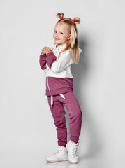 Little happy smiling girl posing in sportswear and sneakers on gray background.