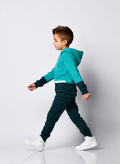 Little brunette boy in a sports suit posing on a gray background.