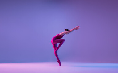 Beautiful. Young and graceful ballet dancer isolated on purple studio background in neon light. Art, motion, action, flexibility, inspiration concept. Flexible caucasian ballet dancer, weightless