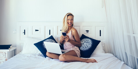 Joyful lady using devices with cute smile in bedroom