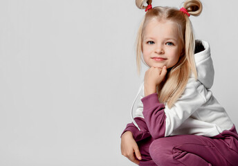 Smiling little blonde girl sitting and looking at the camera on a gray background.