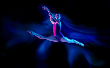 Ghost. Young and graceful ballet dancer on black studio background in neon mixed light. Art, motion, action, flexibility, inspiration concept. Flexible caucasian ballet dancer, weightless jumps.