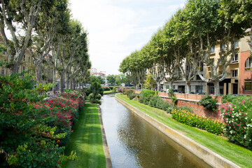 The beautiful water canal (small river) flowing through the beautiful medieval city of Perpignan, France, with its blossoming garden and traditional architecture