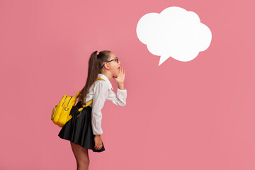 Shares a secret. Preschooler girl in uniform with backpack says whisper to abstract cloud for words