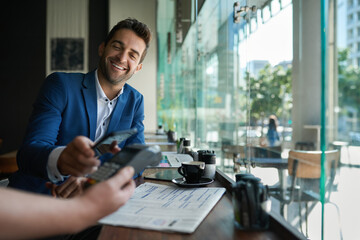Smiling man paying his cafe waiter using nfc technology