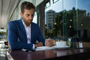 Businessman writing in a notebook at a sidewalk cafe table