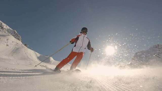 SLOW MOTION FOLLOW Extreme young skier with helmet skiing in perfect early morning cold winter day on a fresh groomed piste at the ski resort. Sun flare is shinning above the fog in the valley