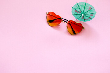 heart shape sunglasses and paper cocktail umbrella on pink background