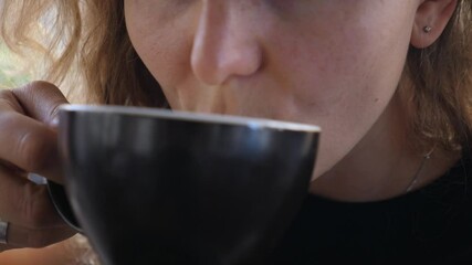 Close up of girl enjoying a sip of warm cappuccino in black mug . Latte art concept