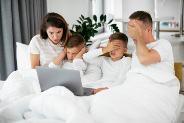 Beautiful parents with kids enjoying at home. Young family watching movie on lap top..