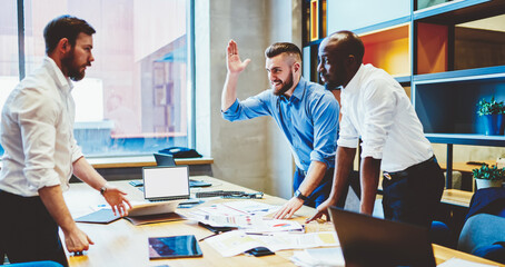 Multiracial crew of financial experts communicating at office table while analyzing strategy, formally dressed business partners discussing sponsorship brainstorming at desk with mockup laptop