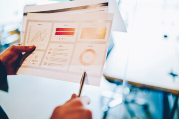 Cropped image of man holding paper with revenue diagram for project accountings, economist pointing on infographic document with marketing analytic of corporate income and development results