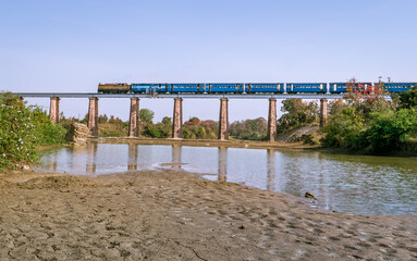 Narrow gauge train crossing Marhu river bridge with river.