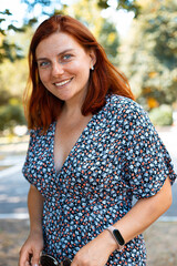 Vertical photo of cute red-haired girl in smiling and looking at the camera in the park