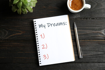 Notebook with dreams list on dark wooden table, flat lay