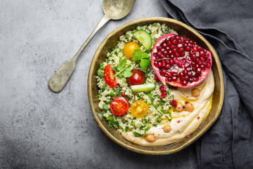 Rustic bowl with couscous salad with vegetables, hummus and fresh cut pomegranate. Middle eastern or Arab style meal with seasonings and fresh cilantro. Healthy Mediterranean dinner, space for text.