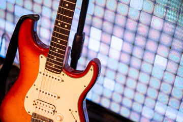 An electronic guitar stands on stage against the backdrop of light panels. CONCERT BEGINNING, SCHEDULE MUSICAL PERFORMANCE.