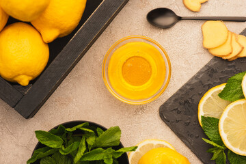 top view of yellow lemons, mint green leaves, ginger root slices and honey on beige concrete surface
