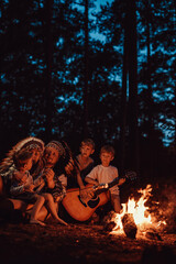 Caring mother and father from USA playing guitar and cooking treat. Family relaxing near bonfire and camping in the wood.