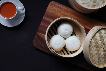 pork and egg creamy steam buns are in the dim sum basket and served on the black wooden table with cup of milk tea in Chinese Cantonese restaurant during tea time yum cha