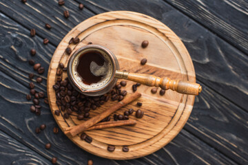 top view of cezve with coffee near cinnamon sticks on wooden board