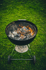 Round mobile weber grill or barbecue parked on a green surface or lawn. Visible flame and fire on a...