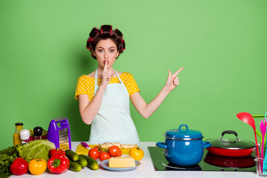 Astonished Girl Chef Point Index Finger Copyspace Lips Mouth Dont Share Secret Dish Dinner Prepare Wear Yellow Dotted T-shirt Hair Rollers Tomato Pepper Isolated Green Color Background