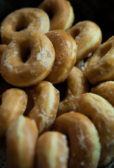 Pile of delicious sugar glazed donuts or doughnuts, with dark background and selective focus, indulgent sugary dessert, sweet treat accompanying a breakfast hot beverage, or a cheat day snack