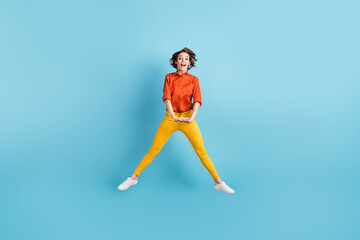 Fototapeta na wymiar Full size photo of pretty crazy funky lady jump high up good mood spend summer holidays vacation free time wear orange shirt yellow trousers sneakers isolated blue color background
