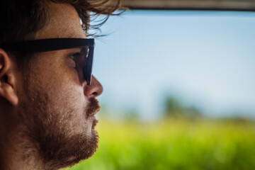 Side or profile picture of a young male man driving a car with the open window exposing the green fields and blue sky. Vintage effect picture with retro bokeh