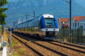 A fast commuter passenger train in France in blue and silver color, traveling on a two track line just close to the station of Moirans Galifette on a sunny day.