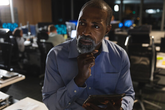 Thoughtful senior Black African American businessman using digital tablet at modern office