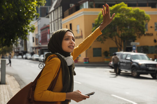 Woman in hijab hailing a taxi on the street - Powered by Adobe
