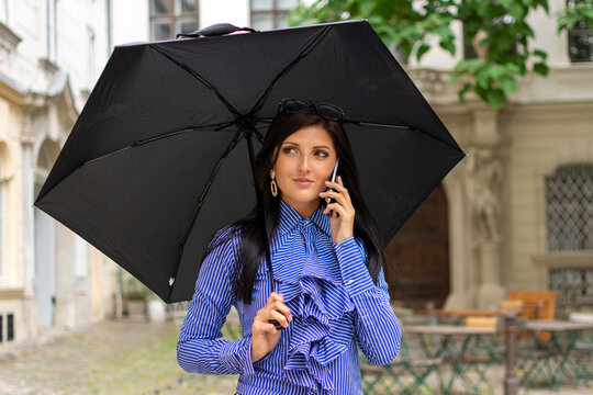 Image of a beautiful stylish woman on a rainy summer day with an umbrella talking on a mobile phone