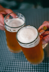 Close-up view of a two glass of beer in hand. Beer glasses clinking at bar or pub