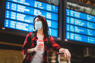 Young woman wearing protective face mask standing information panel at airport or train station