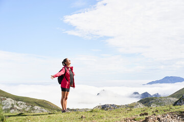 Woman with backpack standing and with open arms on top of a mountain and looking somewhere