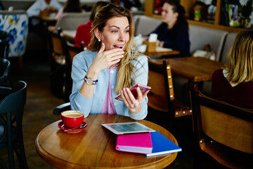 Surprised young woman using smartphone during coffee break in cafeteria