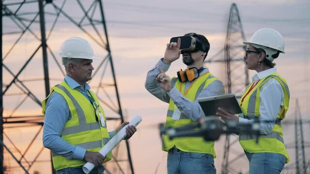 Electric industry, electrical energy production concept. Engineers work with VR equipment and drones in a field.