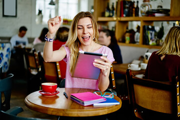 Excited young woman using tablet in cafe
