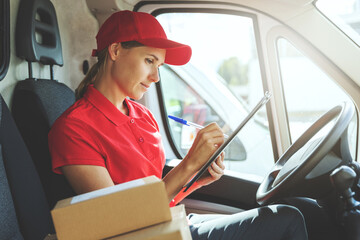 delivery woman in red uniform sitting in van and writing documents