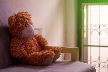Teddy bear representative of a child wearing a face mask, sitting and looking out the window with loneliness and Sadness. Coronavirus Covid-19 and pm2.5, stay at home, quarantine concept.