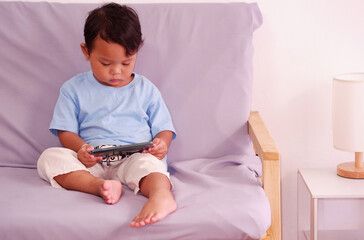 Cute asian about 2 years old, watching and playing mobile phone sits on the sofa in the living room.