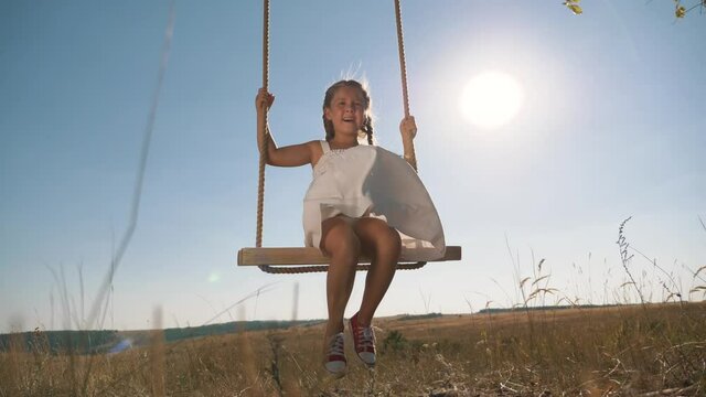 Amusement park dream concept. Happy girl swinging on a swing in the park at sunset. child plays with wooden swing, childhood dream, airplane pilot flights to the sky. A happy family