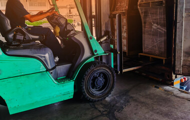 Fototapeta na wymiar Worker driving forklift loading shipment carton boxes goods on wooden pallet at loading dock from container truck to warehouse cargo storage in freight logistics, transportation industrial, delivery