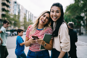 Half length portrait of cheerful female friends smiling at camera during together travel vacations, happy diverse hipster girls satisfied with sincerely friendship relations posing at urban street