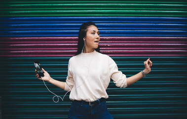 Carefree millennial female in digital headphones enjoying electronic music for dance near publicity...
